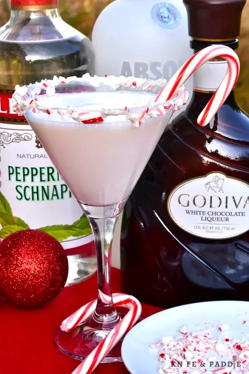 Peppernint schnapps, Godiva White Chocolate Liqueur, vodka combined and poured in a candy cane rimed glass and a candy cane for garnish