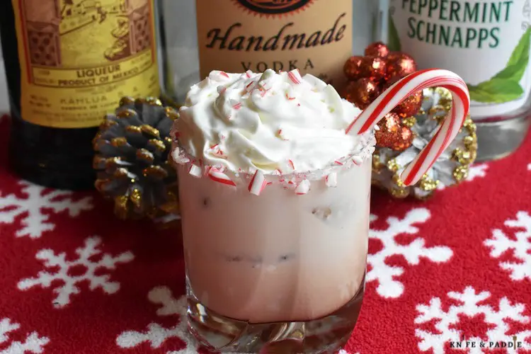 Peppermint White Russian in a lowball glass rimmed with crushed candy canes and topped with whipped cream, crushed candy canes and a candy cane for garnish