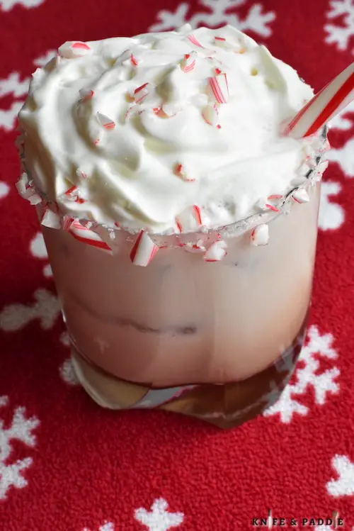 Peppermint White Russian in a lowball glass rimmed with crushed candy canes and topped with whipped cream, crushed candy canes and a candy cane for garnish