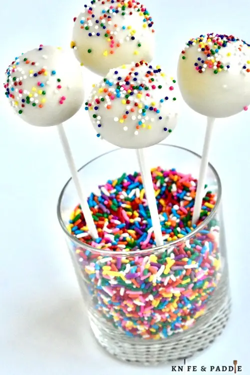 Cake pops with festive nonpareils  in a glass filled with sprinkles