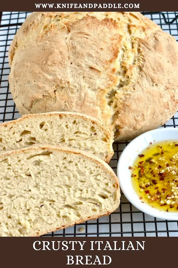 Crusty Italian bread sliced and in loaf form on a wire rack with olive oil for dipping 