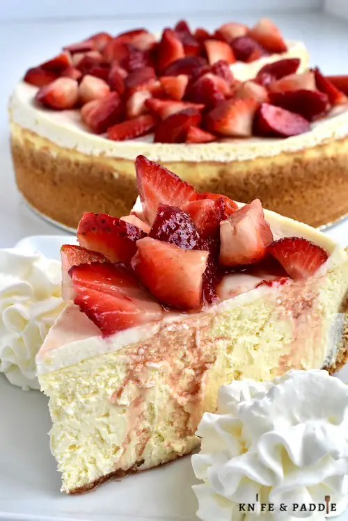 Slice of cheesecake topped with fresh strawberries and whipped cream