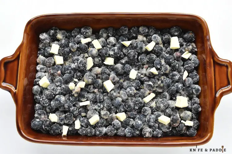 Blueberry mixture in a baking dish dotted with butter