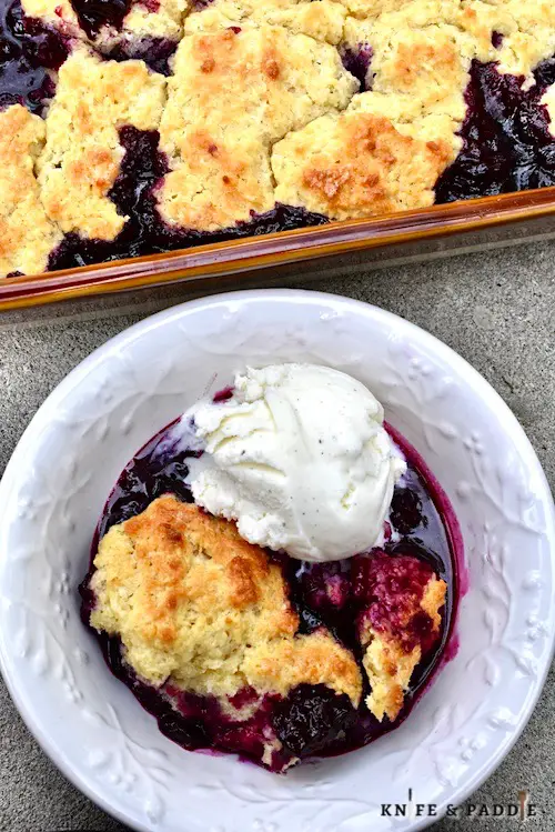 Irresistible Blueberry Cobbler in a baking dish and in a bowl topped with vanilla ice cream