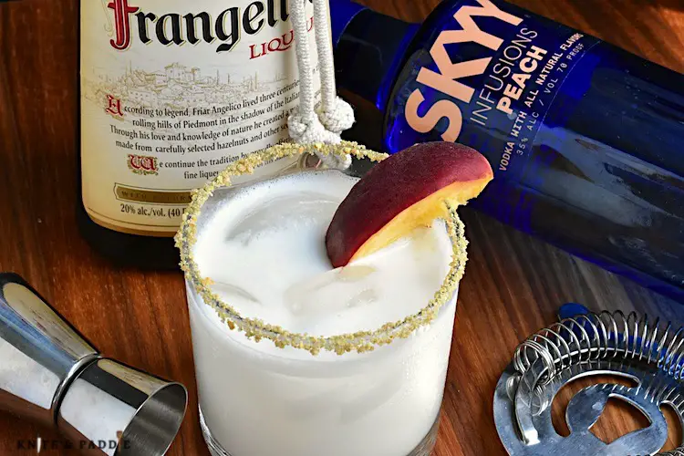 Peach Cobbler Cocktail served in a lowball glass with ice garnished with a graham cracker and brown sugar rim and a peach slice