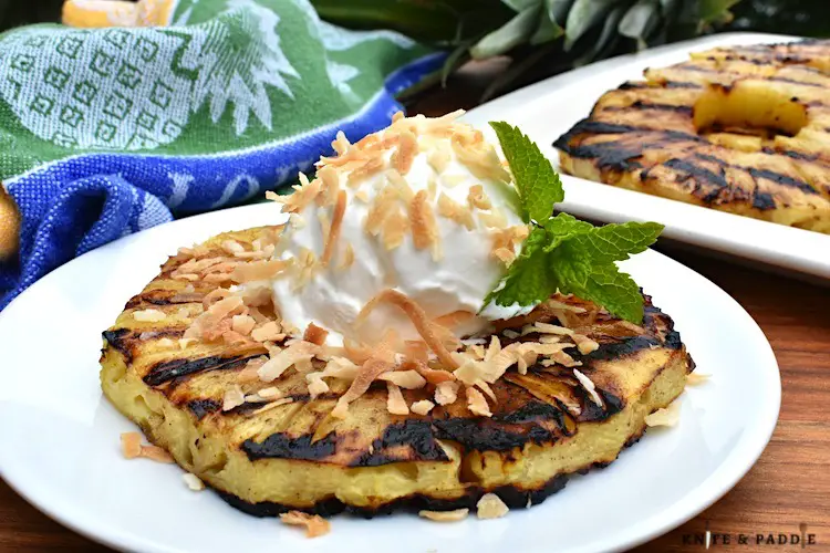 Piña Colada Grilled Pineapple on a plate with coconut whipped topping and toasted shredded coconut 