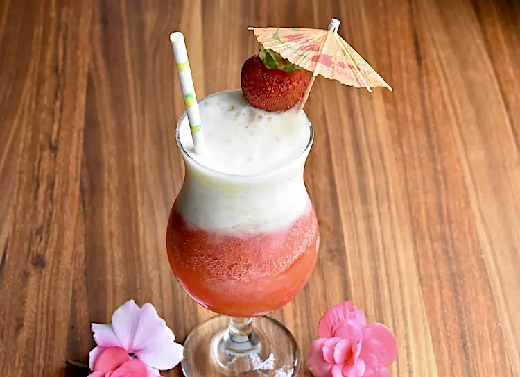 The Miami Vice Cocktail in a hurricane glass garnished with a fresh strawberry and a cocktail umbrella