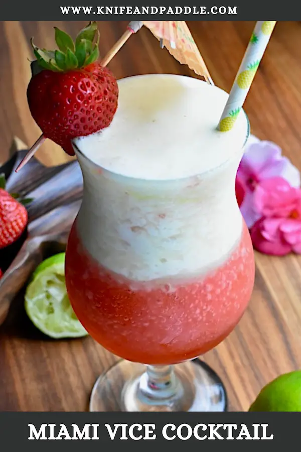 Layered piña colada and strawberry daiquiri cocktail in a hurricane glass garnished with a fresh strawberry and a cocktail umbrella