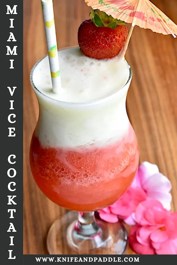 Layered piña colada and strawberry daiquiri cocktail in a hurricane glass garnished with a fresh strawberry and a cocktail umbrella