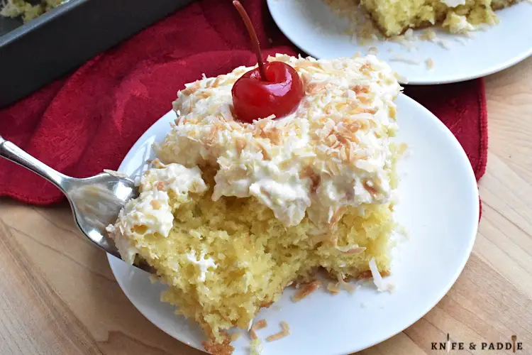 Tropical dessert made with a yellow box cake topped with a crushed pineapple and whipped topping frosting, toasted coconut and a maraschino cherry