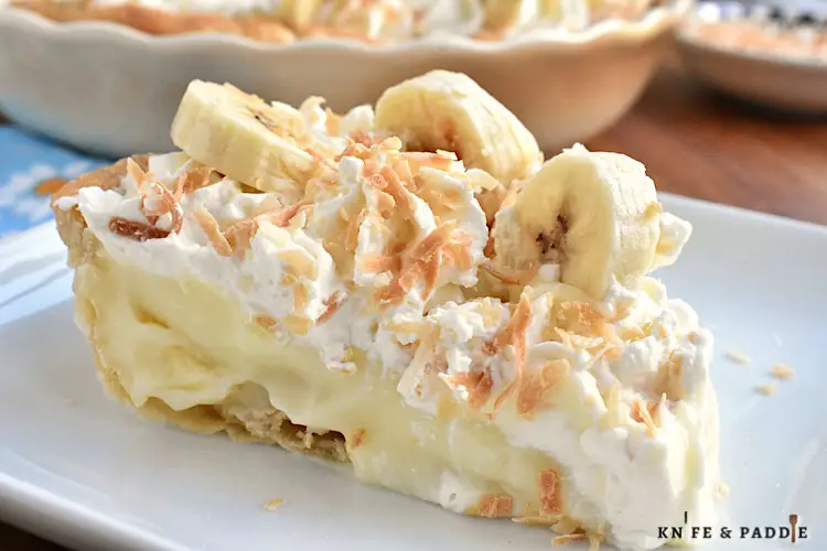 Slice of classic Banana Cream Pie topped with homemade whipped cream, fresh bananas and toasted coconut