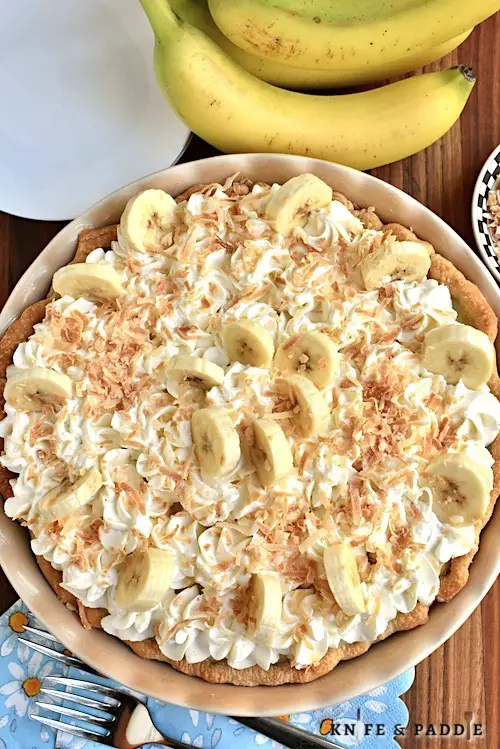 Vanilla pudding in a golden brown pie shell topped with toasted coconut and whipped cream