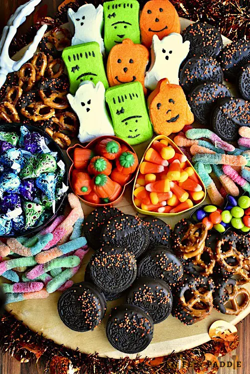 Halloween Charcuterie Board filled with Ghost, Frankenstein and Pumpkin Pepps, Pretzels, Candy Corn, Pumpkin Candy Corn, Gummy worms, M&M's, Oreos, Hershey's Kisses arranged on a platter