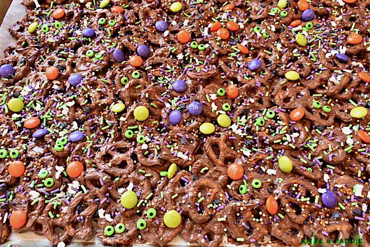 Easy salty, sweet and crunchy candy topped with orange, purple and green M&M's, green candy eyeballs, candy bones, candy spiders and purple, green and white sprinkles spread on a baking sheet