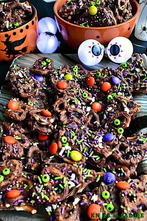 Easy salty, sweet and crunchy candy topped with orange, purple and green M&M's, green candy eyeballs, candy bones, candy spiders and purple, green and white sprinkles