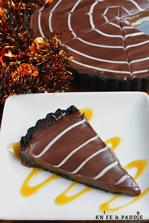 Slice of Halloween No-Bake Salted Caramel Tart with an Oreo crust and a white chocolate spider web ganache