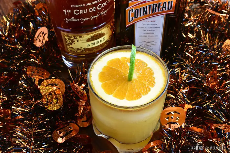 Jack O' Lantern Cocktail made with cognac, cointreau, orange juice and ginger ale mixed together to create a festive Halloween cocktail garnished with a pumpkin made from a slice of orange and a lime peel