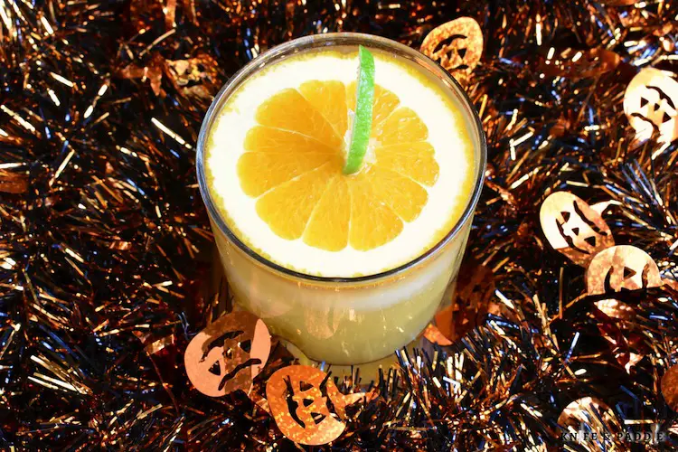 Jack O' Lantern Cocktail with a slice of orange and a lime peel