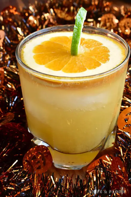 Jack O' Lantern Cocktail made with cognac, cointreau, orange juice and ginger ale mixed together to create a festive Halloween cocktail garnished with a pumpkin made from a slice of orange and a lime peel