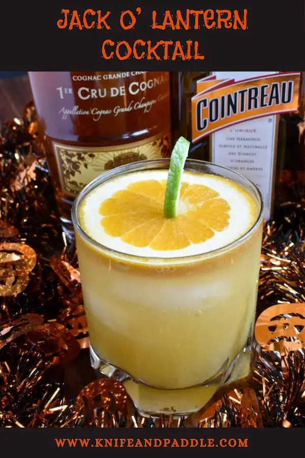 Jack O' Lantern Cocktail made with cognac, cointreau, orange juice and ginger ale mixed together to create a festive Halloween cocktail garnished with a pumpkin made from a slice of orange and a lime peel