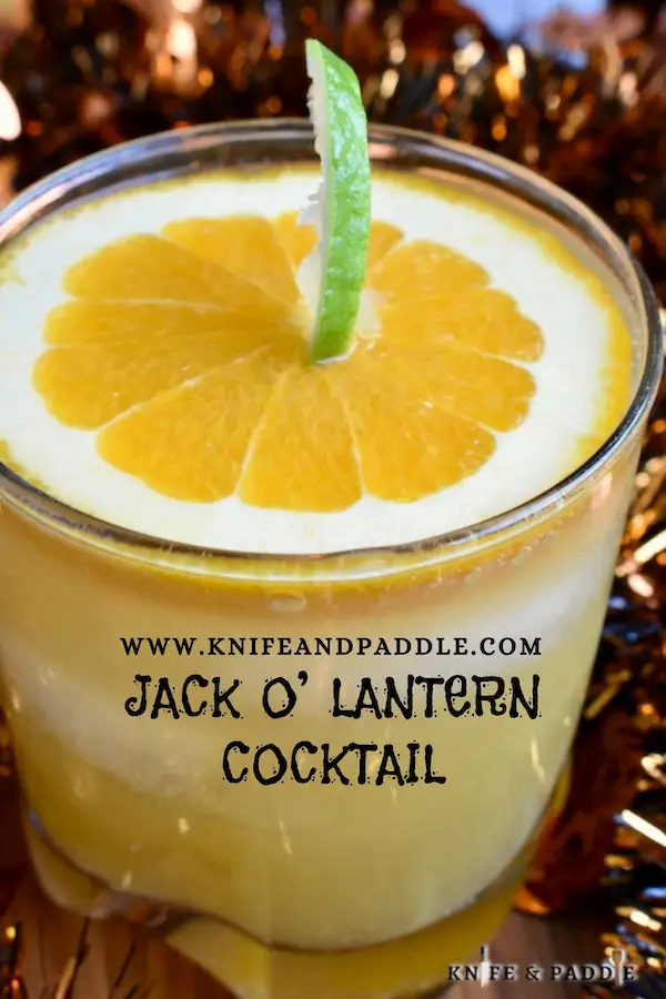 Cognac, Cointreau, orange juice and ginger ale mixed together to create a festive Halloween cocktail garnished with a pumpkin made from a slice of orange and a lime peel