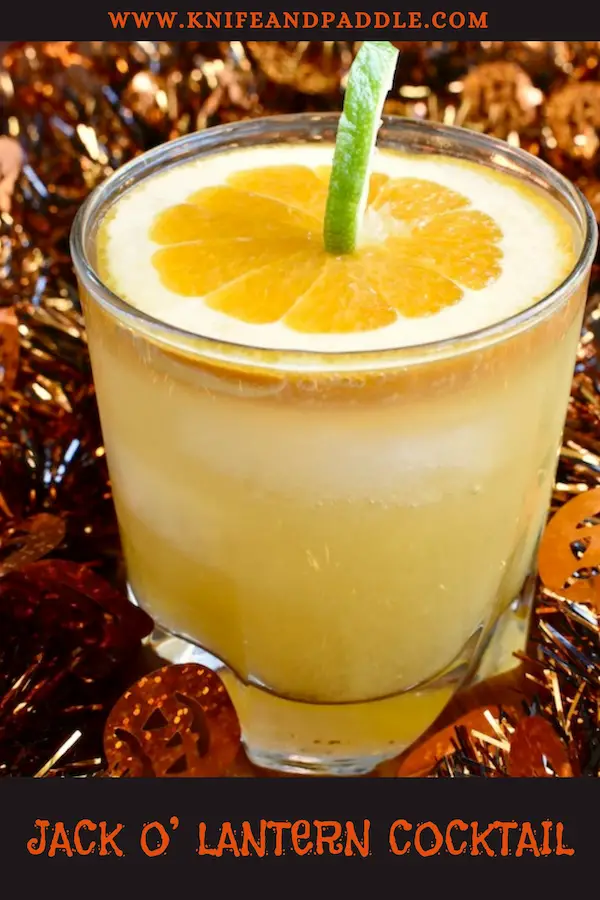 Cognac, Cointreau, orange juice and ginger ale mixed together to create a festive Halloween cocktail garnished with a pumpkin made from a slice of orange and a lime peel