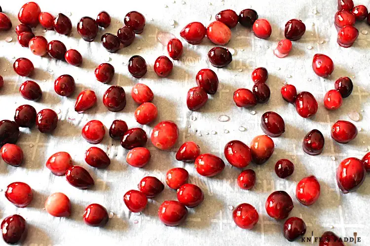 Fresh cranberries coated in simple syrup on a parchment lined baking sheet